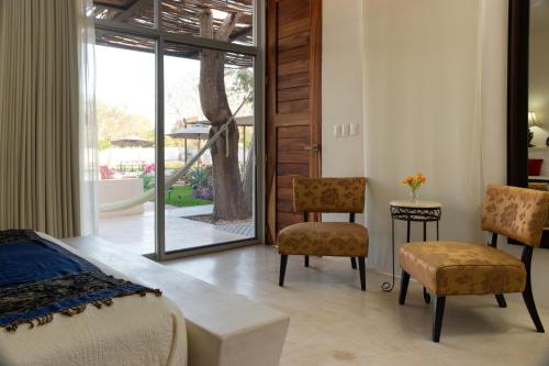 a bedroom with a bed and chairs and a sliding glass door at Hotel Casa de Campo Conkal Merida in Conkal