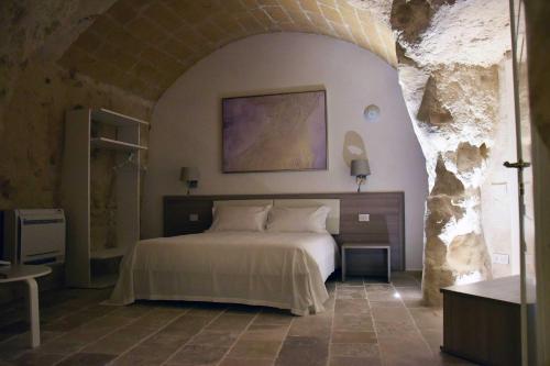a bedroom with a white bed in a stone wall at 5 Elementi Sassi Matera in Matera