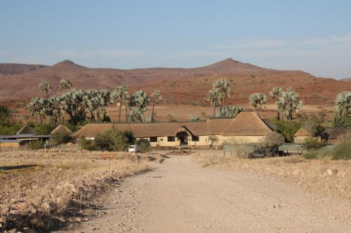a dirt road through a village with mountains in the background at Palmwag Lodge in Palm