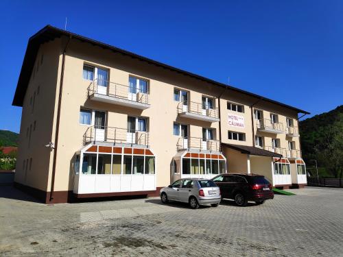 a large building with two cars parked in a parking lot at Hostel Caliman in Caciulata
