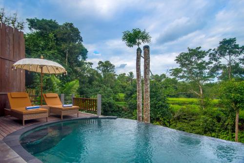 a swimming pool with two chairs and an umbrella at Alam Dania Cottage in Ubud