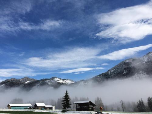 a group of houses in a field with fog in the mountains at Ferienwohnung Lassendorf in Hermagor