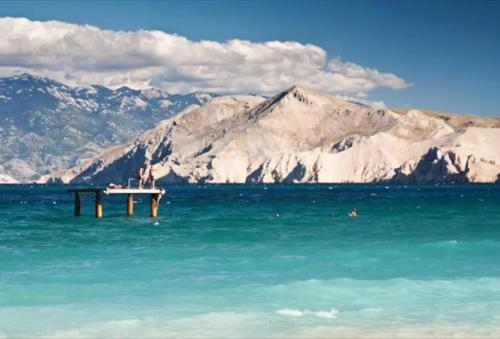 a pier in the middle of the water with a mountain at Apartman Valdi in Baška