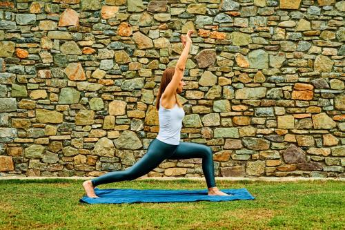 a woman doing a yoga pose in front of a stone wall at Nectar luxury apartments in Sitia