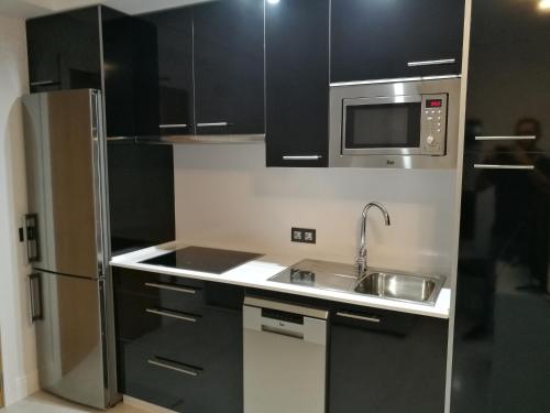 a kitchen with black cabinets and a stainless steel refrigerator at Apartamentos Las Palmeras in Palma del Río