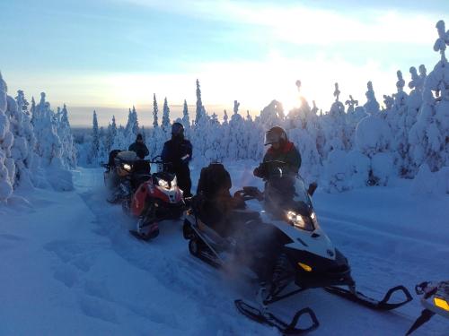 um grupo de pessoas andando de moto na neve em Ollilan Lomamajat em Kuusamo