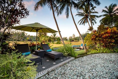 a patio with two chairs and an umbrella and palm trees at Villa Taman di Blayu by Nagisa Bali in Tabanan