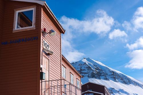 a building with a snow covered mountain in the background at Gjestehuset 102 in Longyearbyen