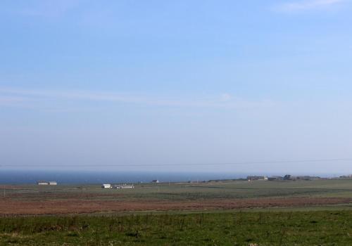 a large field with a field of grass and the ocean at Hillside Camping Pods and Shepherd's Hut in Wick