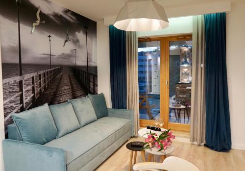 a living room with a blue couch and a painting of a pier at Apartament Batorego 713 in Gdynia