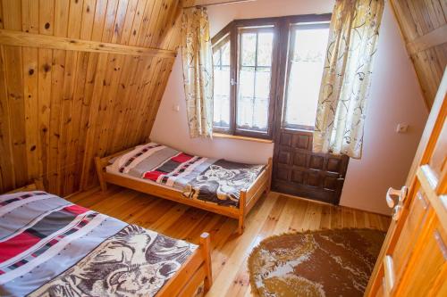 two beds in a room with wooden walls and a window at Domek na Mazurach Pasym in Pasym