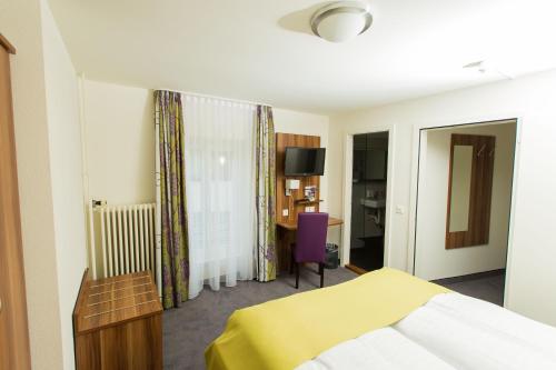 Habitación de hotel con cama amarilla y escritorio. en Hotel Restaurant Resslirytti, en Basilea