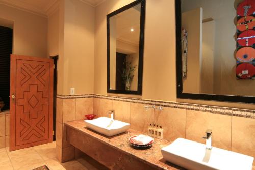 a bathroom with two sinks and two mirrors at AmmaZulu African Palace in Kloof