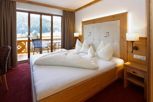 a bedroom with a large white bed with a balcony at Hotel Berghof in Söll