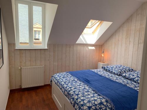 a bedroom with a bed with a blue comforter and two windows at Clos des Ursulines in Bayeux