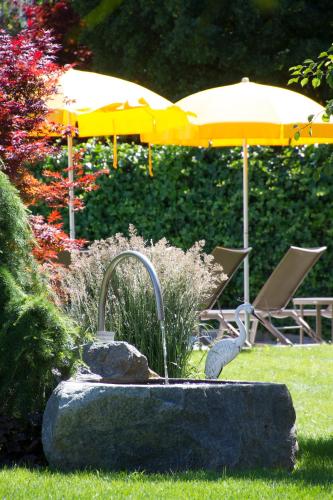 a fountain in a garden with an umbrella and chairs at Pension Sattlerenglhof in Laces