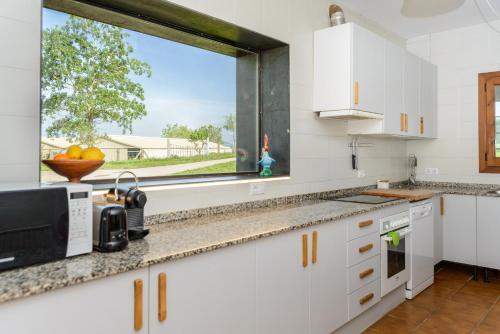 a kitchen with white cabinets and a large window at Cal Menescal in Les Olives