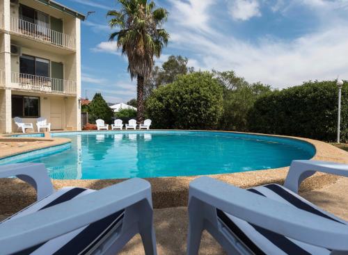 a swimming pool with two chairs in front of a building at Harriet House Tumut in Tumut