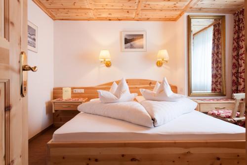 a bedroom with a bed with white sheets and pillows at Hotel Enzian in Zürs am Arlberg