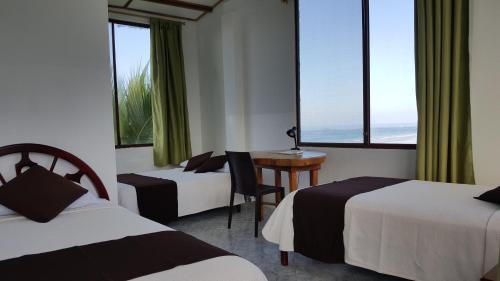 a hotel room with two beds and a desk and windows at Hotel La Jungla in Puerto Villamil