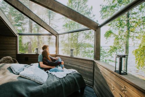 a woman sitting on a bed in a room with a window at Revontuli Resort Glass Igloos in Hankasalmi