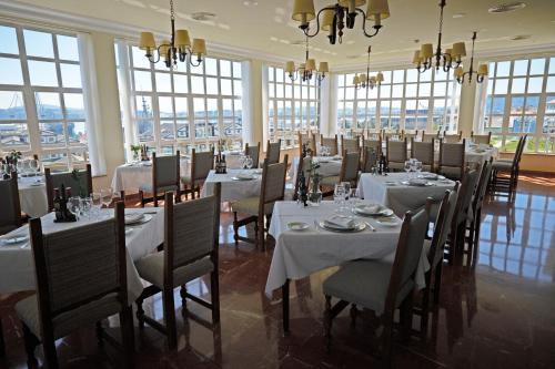 a dining room with white tables and chairs and windows at Parador de Ferrol in Ferrol
