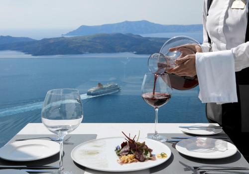 a person pouring red wine into a glass at a table with a meal at Petit Palace Suites in Fira