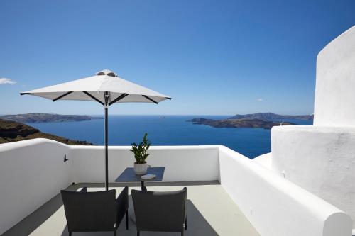 a table with an umbrella on a balcony with the ocean at Petit Palace Suites in Fira
