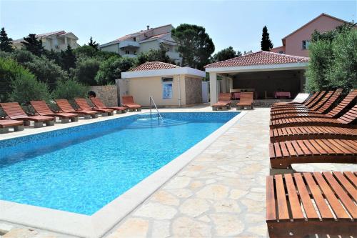 a swimming pool with lounge chairs and a house at Lenka Apartments I in Novalja