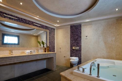 a bathroom with a tub and a toilet and a large mirror at Petit Palace Suites in Fira