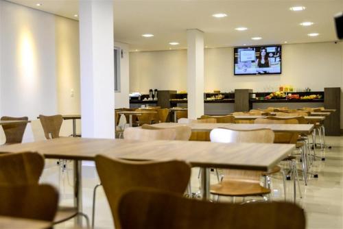 un restaurante con mesas y sillas y TV en la pared en Grand Café Hotel, en Manhuaçu