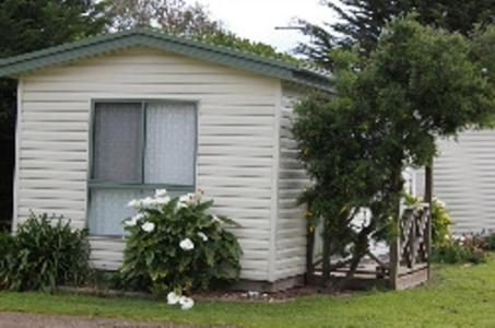 una pequeña casa blanca con una ventana y un árbol en Abel Tasman Cabins Devonport, en Devonport