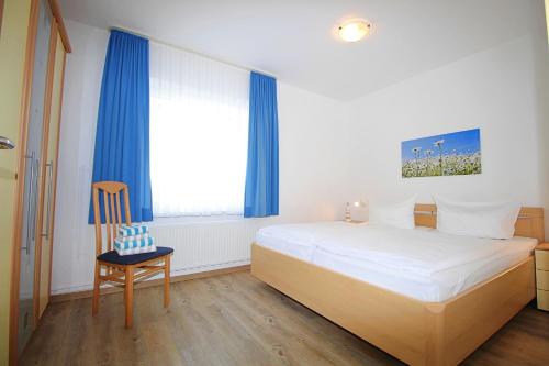 a bedroom with a bed with blue curtains and a chair at Meeresblick Fehmarn in Fehmarn