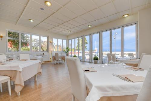 un restaurant avec des tables blanches, des chaises et des fenêtres dans l'établissement Hotel Villa Garuti, à Padenghe sul Garda