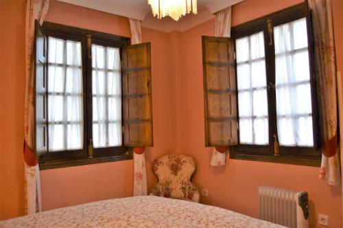 a bedroom with three windows and a chair and a bed at Casa Plaza Sierra Grazalema in Grazalema