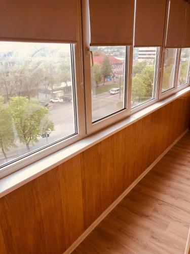 an empty room with three windows and a wooden floor at Classic Apartment in Boryspilʼ
