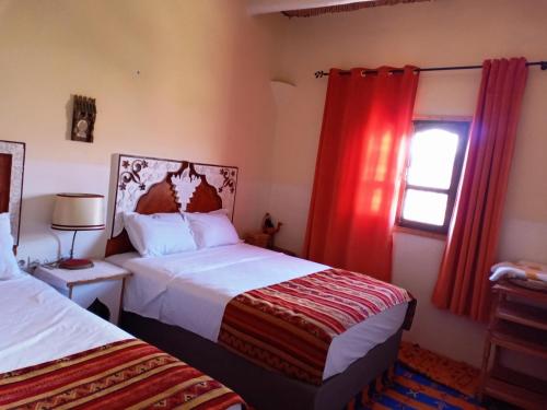 a bedroom with two beds and a window with red curtains at Tizi Maison d'Hôtes in Telouet