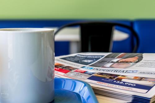 a white coffee cup sitting next to a pile of newspapers at ibis budget Calama in Calama