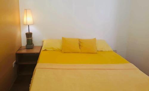 ein Bett mit gelben Laken und einer Lampe auf dem Tisch in der Unterkunft El Pueblo Manila Condominium in Manila
