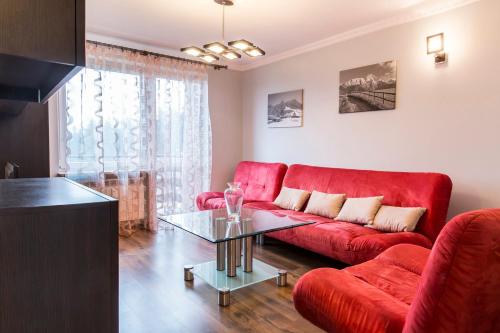 a living room with a red couch and a glass table at Apartament Rubinowy in Kościelisko