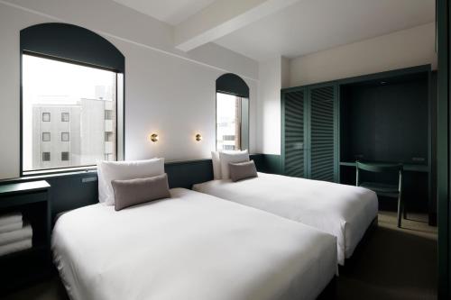 two beds in a hotel room with two windows at DDD HOTEL in Tokyo