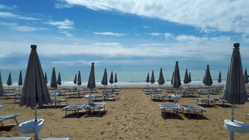 a beach with chairs and umbrellas and the ocean at Hotel Villa Dina in Lido di Jesolo