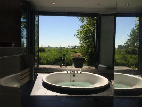 a bathroom with a large tub with a view of a field at Bungalow between Haarlem and Amsterdam with a large bubble bath in Vijfhuizen