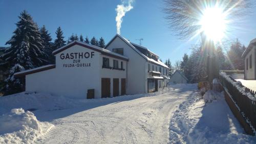 a building on a snowy road with the sun behind it at Genussgasthof Fuldaquelle & Berghof Wasserkuppe in Gersfeld