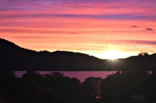 a sunset over a body of water with trees at TOYA HOME kairou 一棟貸切 in Lake Toya