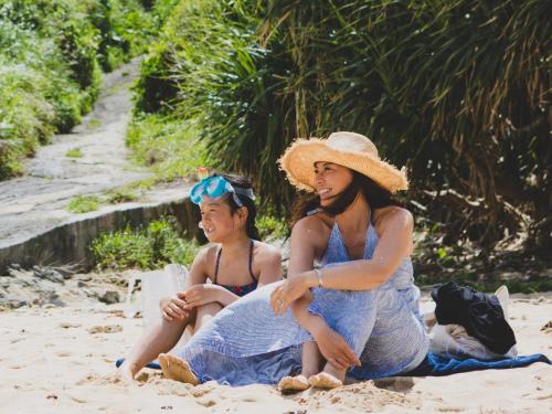 うるま市にあるハイドアウト オキナワ ウルマの砂浜に座る二人の女性