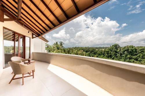 a balcony with a chair and a view of trees at tanadewa Resort Ubud Bali by Cross Collection in Ubud