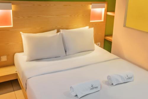 uma cama com lençóis brancos e almofadas num quarto em LeGreen Suite Senayan em Jakarta