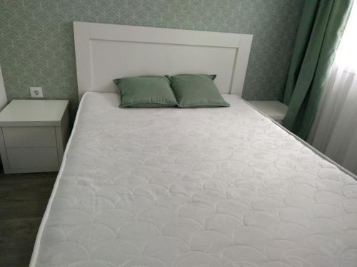a white bed with two green pillows in a bedroom at Apartment Eteri in Batumi