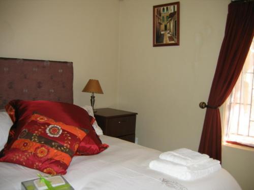 Un dormitorio con una cama con almohadas rojas y una ventana en Malleson Garden Cottage, en Ciudad del Cabo